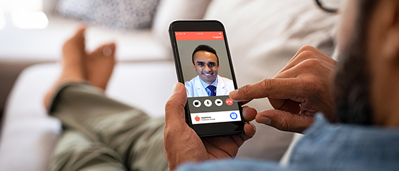 Virtual Care Thumbnail Image Closeup of a man hand holding cellphone with internet browser on screen. Man with spectacles relaxing sitting on couch while looking at mobile phone. Closeup of mature latin man using smartphone to checking email at home.